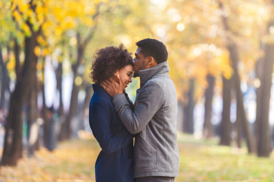 African American Young Man Kissing His Girlfriend Forehead While Walking in a park